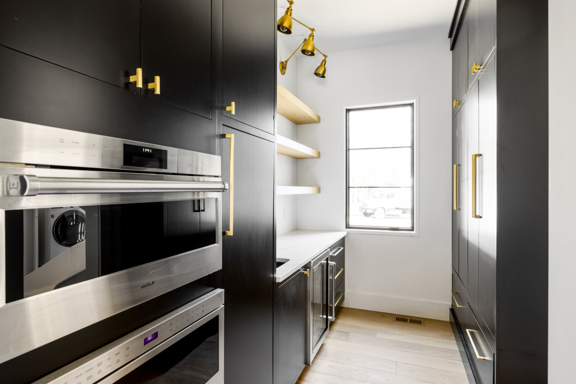 Butler's pantry with black cabinetry, brass hardware and oak floating shelves