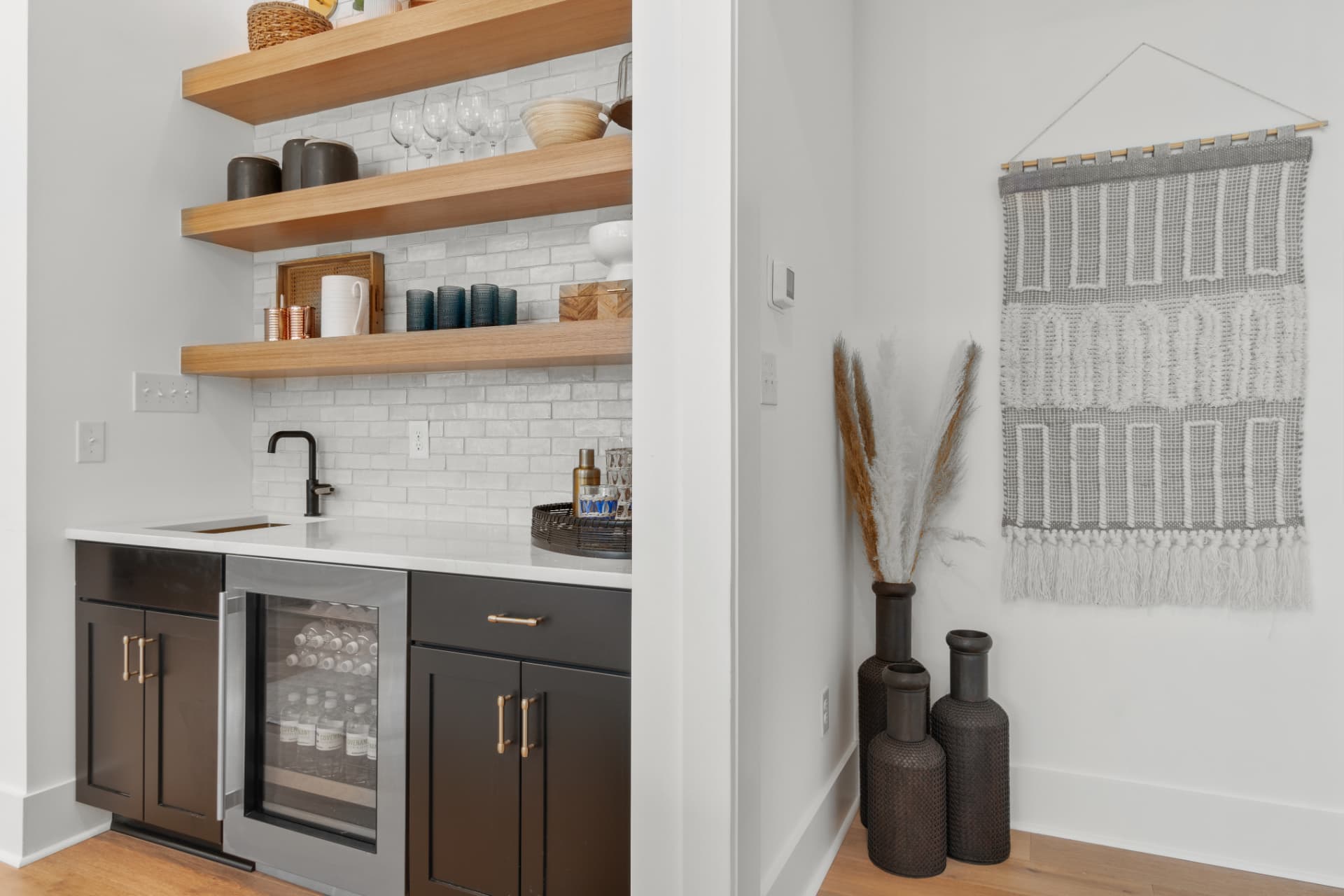 Wet bar with dark base cabinets, wine fridge and oak floating shelves